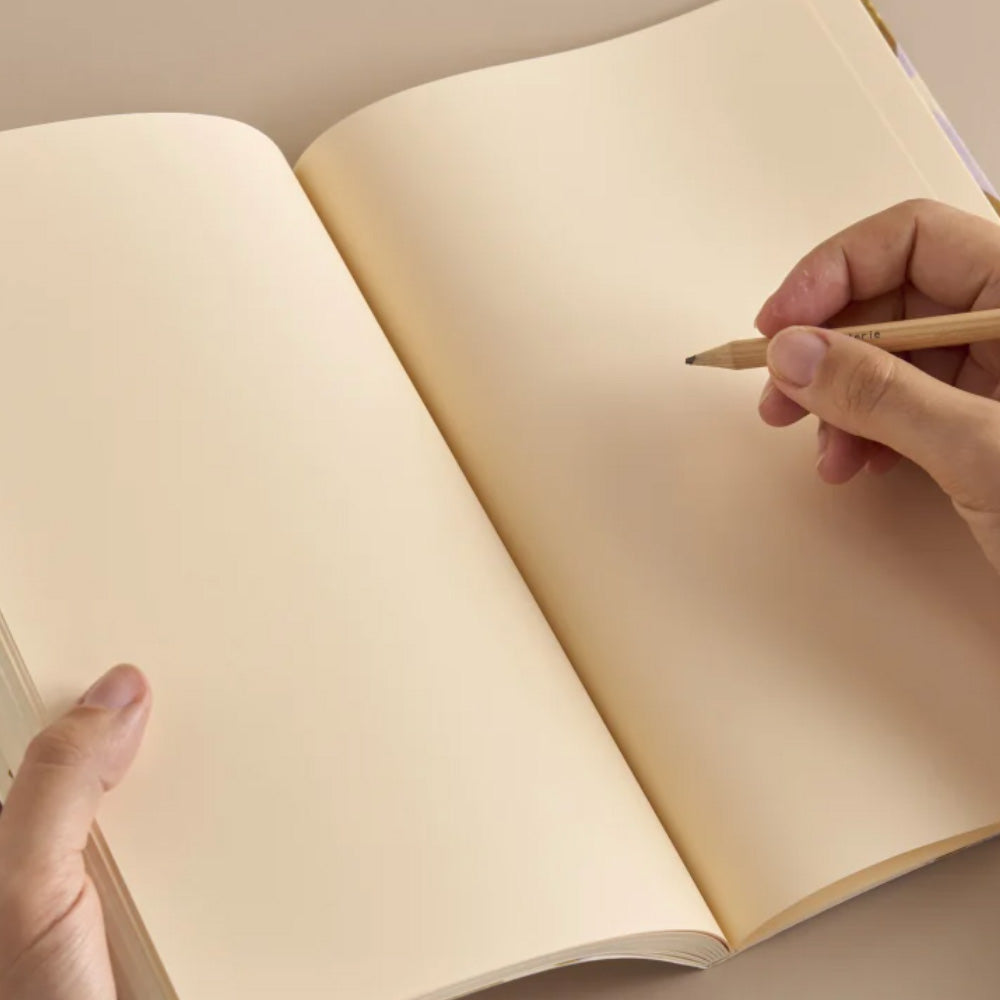 Blank notebook open with a colored pencil in a hand.