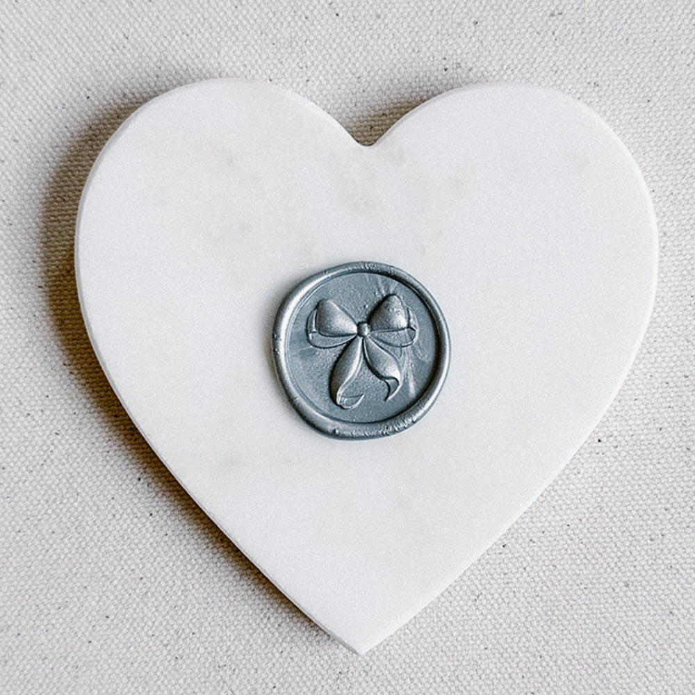 Heart-shaped white stone with a silver bow wax seal on a beige background
