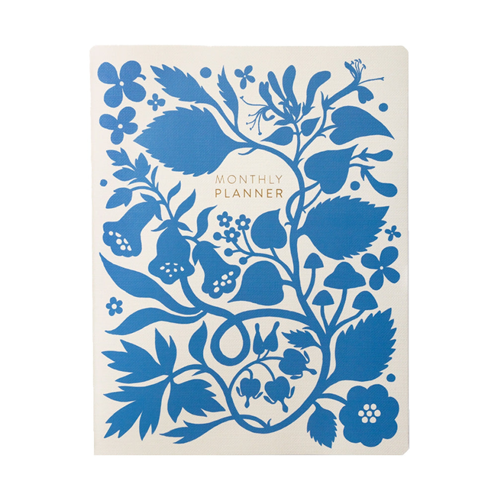 White monthly planner with a blue silhouette of flowers on a connecting stem with the words "MONTHLY PLANNER" in gold foil.