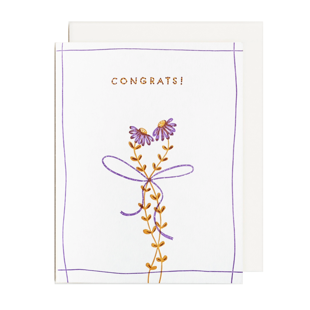 A white congratulations greeting card with a purple border, gold 'CONGRATS!' text, and a purple and gold floral illustration, shown with a white envelope behind it on a light gray background.