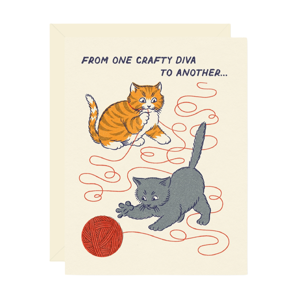 A cream-colored greeting card with a humorous illustration of an orange tabby cat and a gray kitten playing with red yarn, with the text 'FROM ONE CRAFTY DIVA TO ANOTHER.