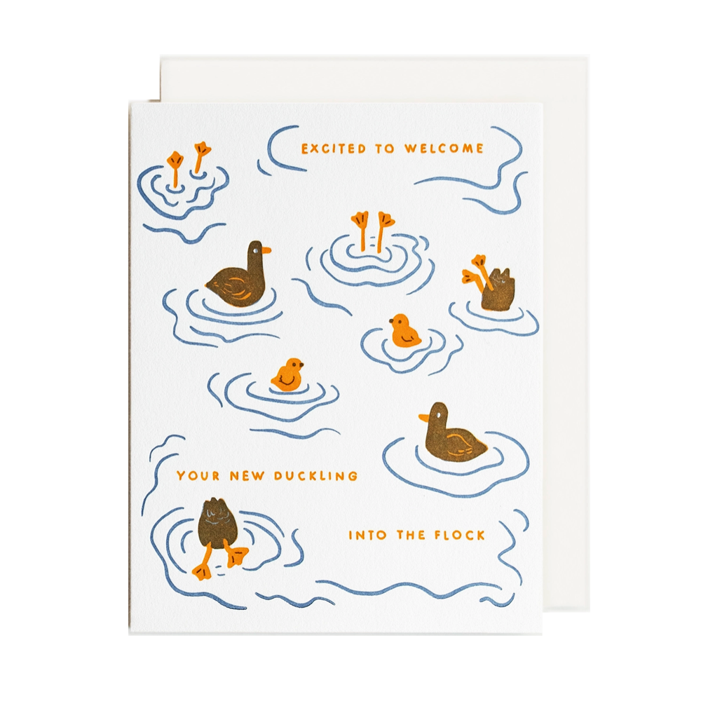 A white greeting card with a cute duck-themed illustration, featuring blue water ripples, brown ducks, and orange text that reads 'EXCITED TO WELCOME YOUR NEW DUCKLING INTO THE FLOCK'. A plain white envelope is partially visible behind the card.