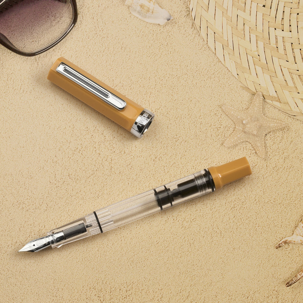 Fountain pen and lighter on sand with sunglasses and shells in the background