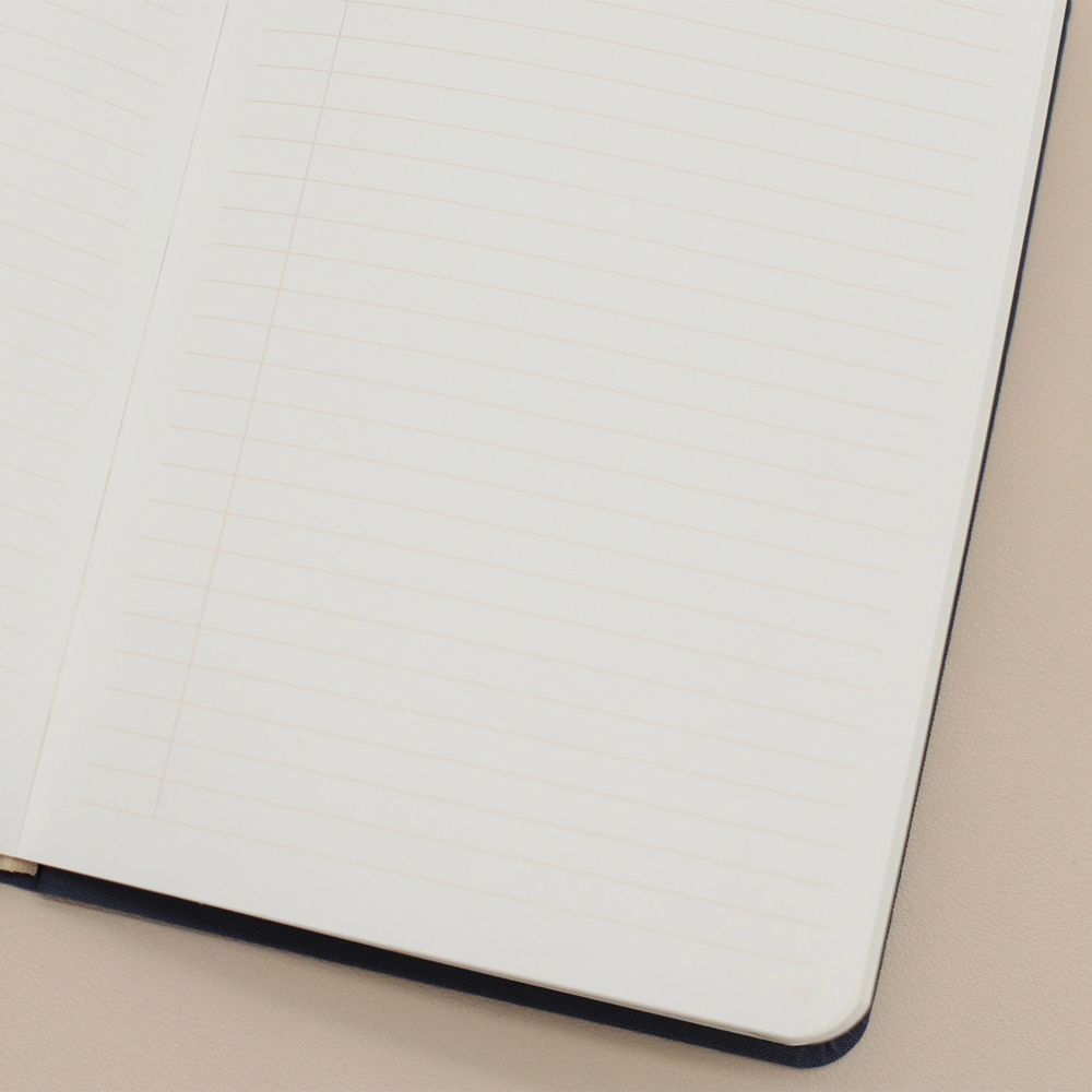 An open lined notebook with white pages and thin light orange horizontal lines, photographed close up on a warm beige surface.