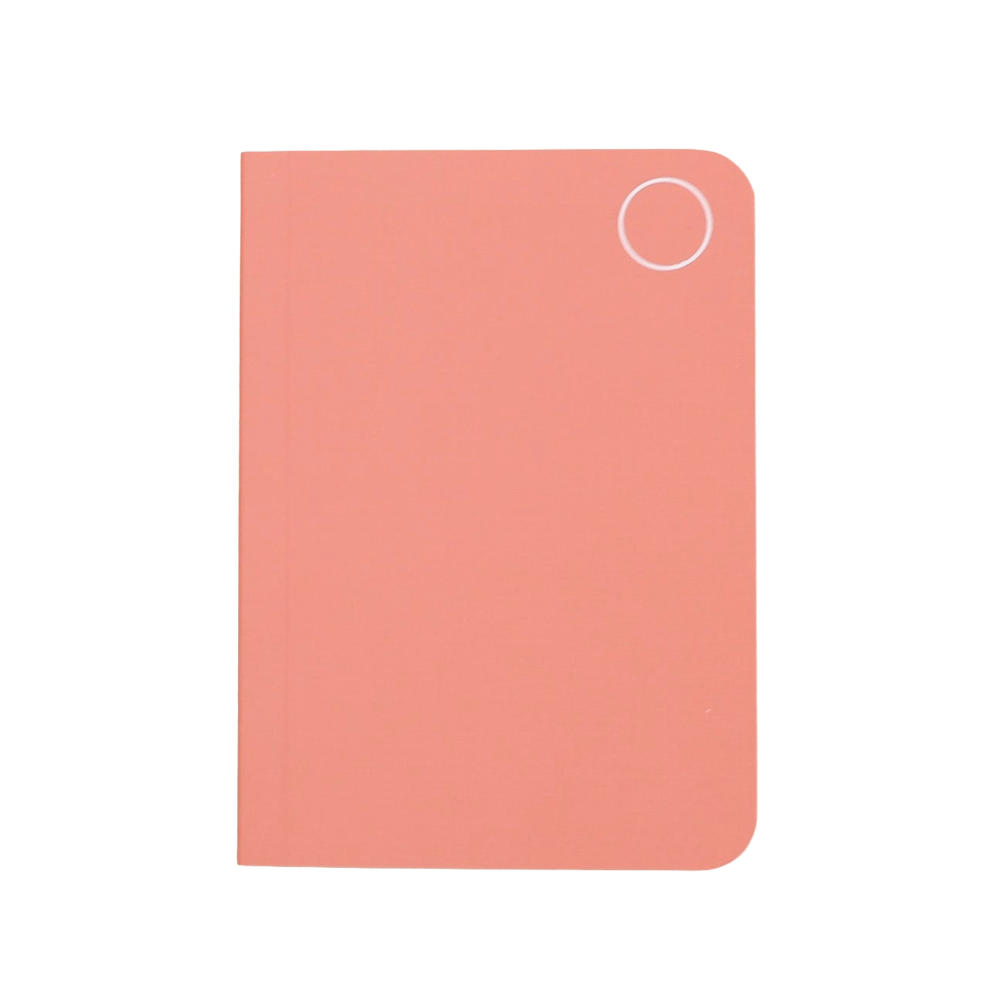 A minimalist, rectangular notebook in a soft coral pink color, featuring rounded corners and a small white circular cutout in the top right corner, shown against a plain white background.