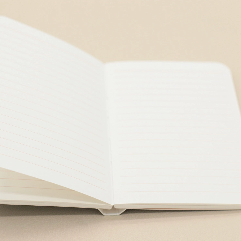 An open lined notebook with blank white pages, photographed on a warm beige background.