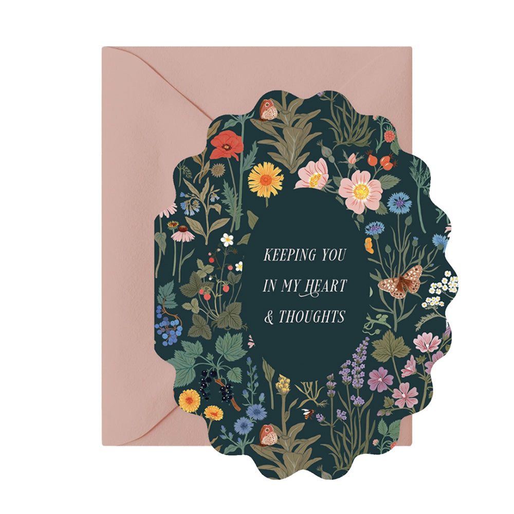 An oval scalloped card with a dark green background. There is a floral design on the background with flowers, plants, and forest animals. The words "Keeping You In My Heart & Thoughts" is in the center in a script font. 
