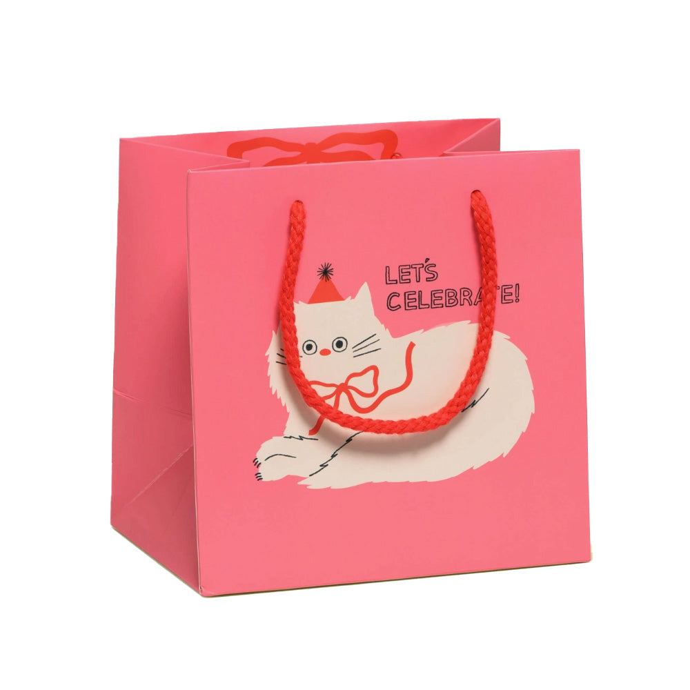 Pink gift bag with a white cat wearing a red bow and red party hat and 'Let's Celebrate!' text on a white background