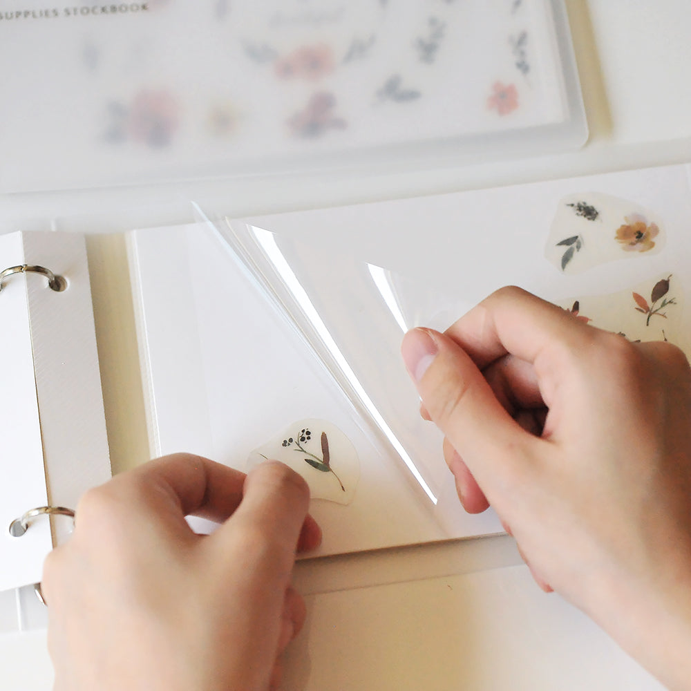Person attaching pressed flowers sticker to a album with a white background