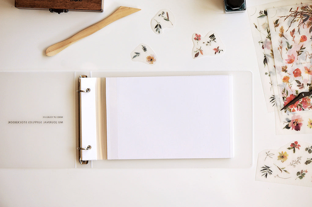 Open notebook with blank page on a white surface with floral decorations