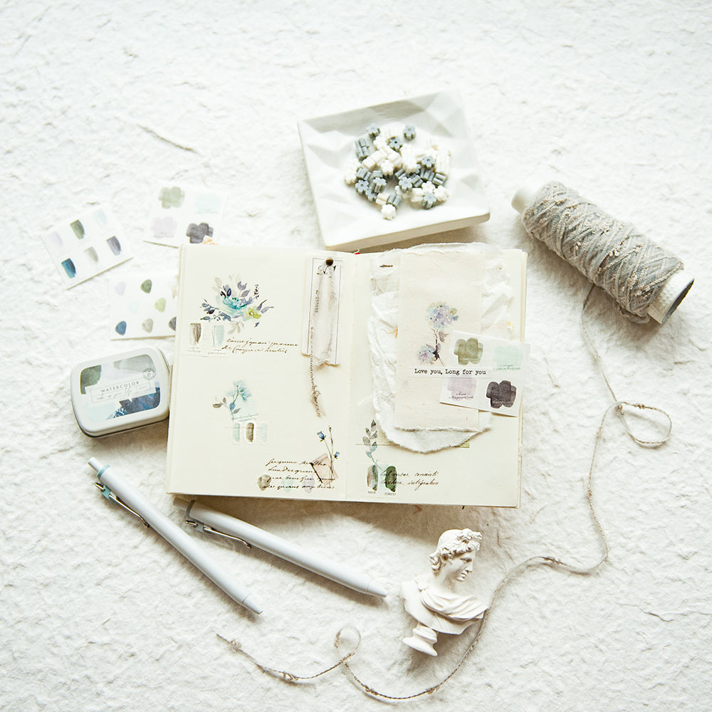 Open notebook with decorative stickers on a textured surface with stationery items.