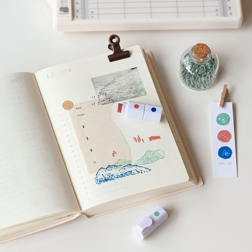 Open notebook with printed designs on a white surface, surrounded by stationery items.