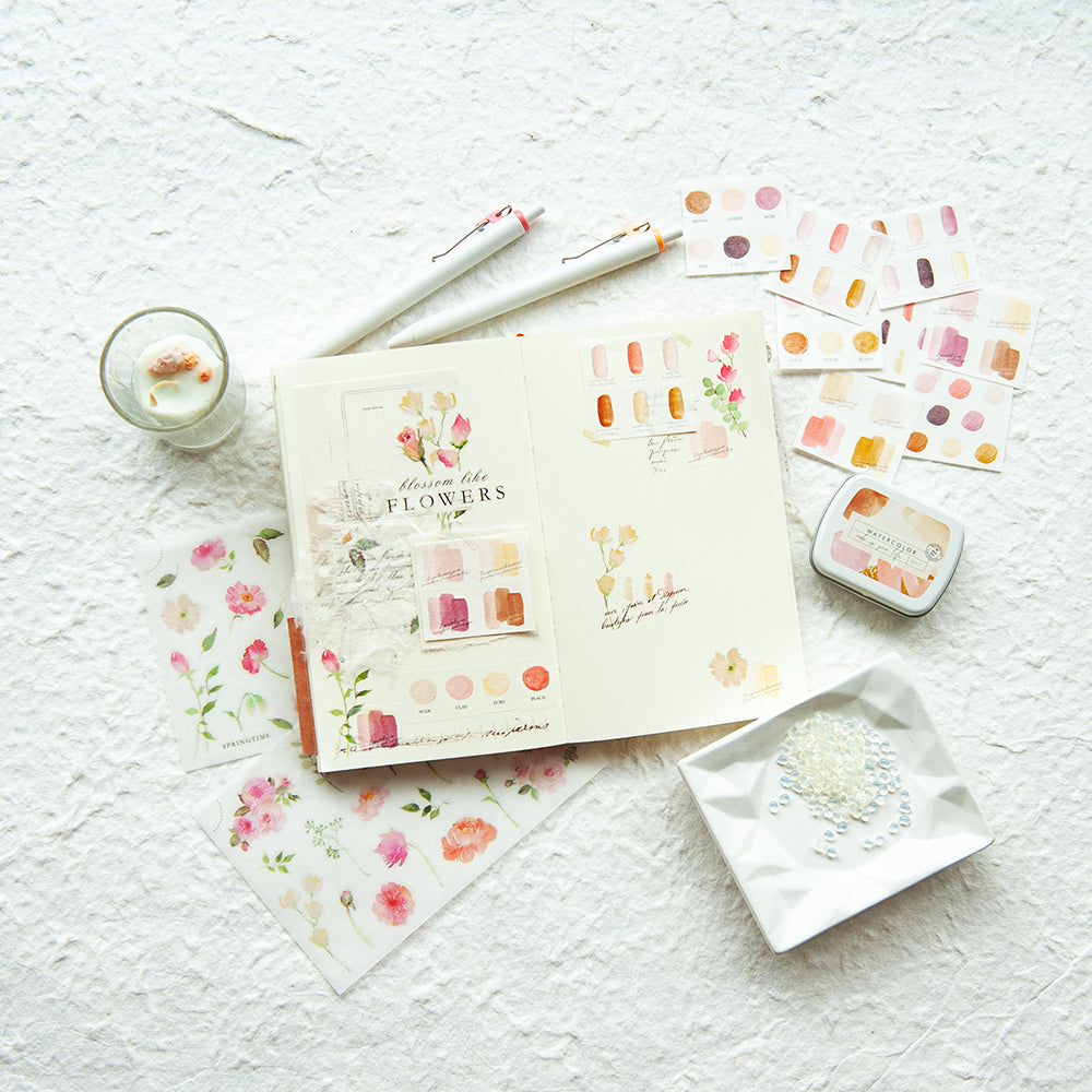 Stationery items including a notebook, pen, and small containers on a textured white surface.