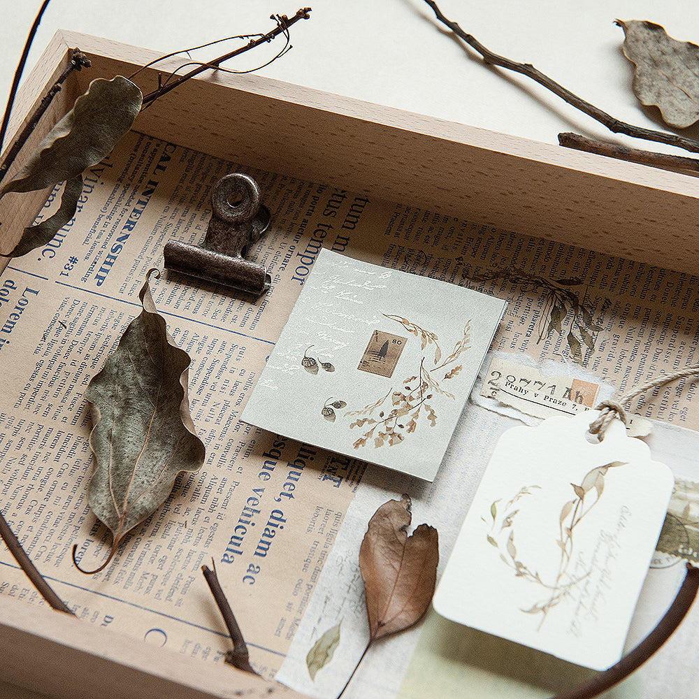 Decorative setting with dried leaves, a clip, and stationery items on an open book with newspaper pages.
