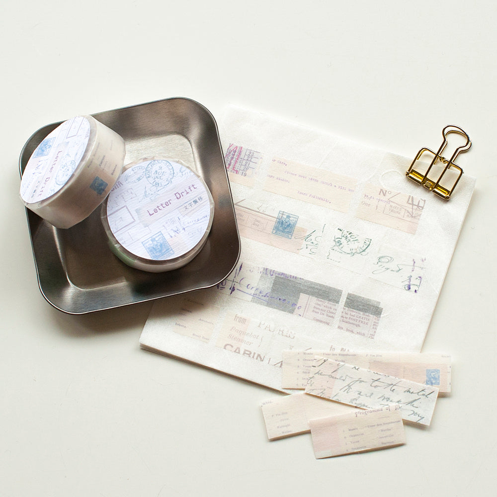 Two containers with lids on a metal tray next to stationery items on a light surface.