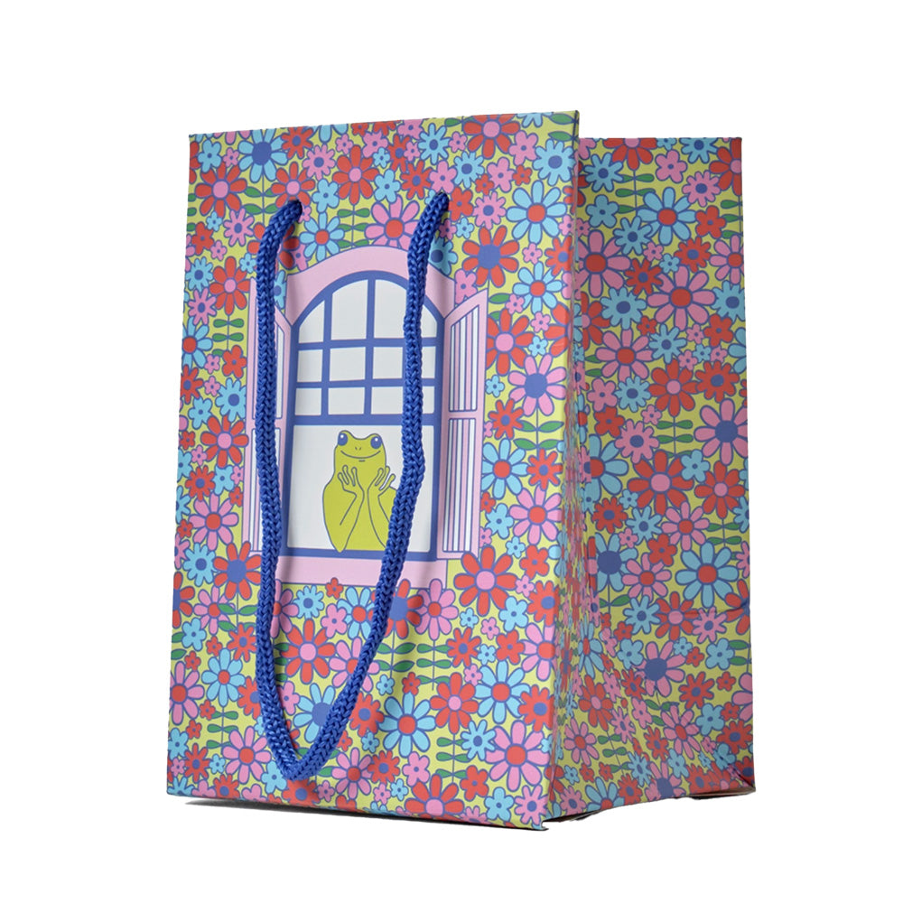 Colorful gift bag with floral pattern and blue handle. Featuring a happy frog looking out of a window.