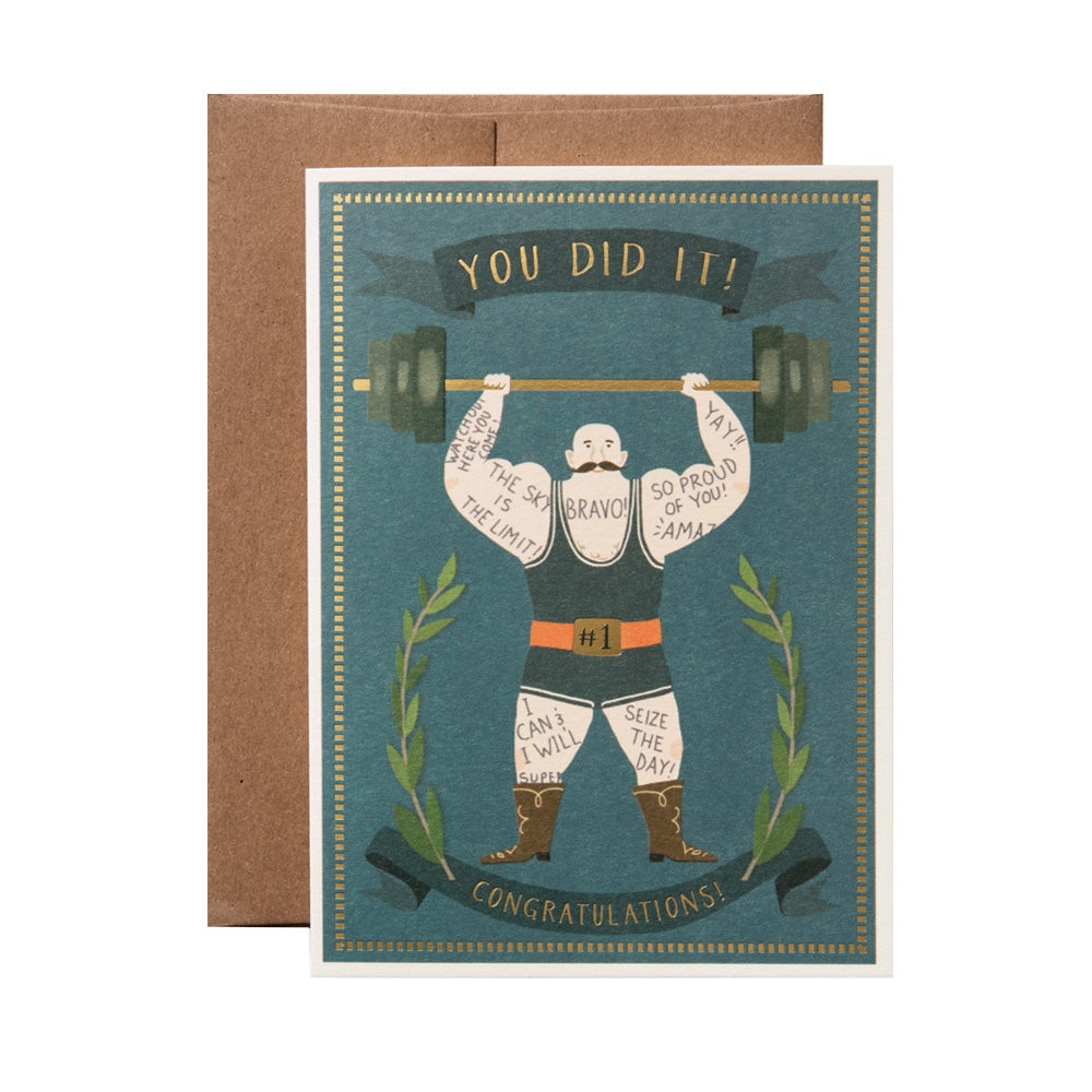Greeting card with a vintage-style illustration of a tattooed strongman lifting weights, text on a banner reading "You did it! Congratulations!" on a blue background with a brown envelope.