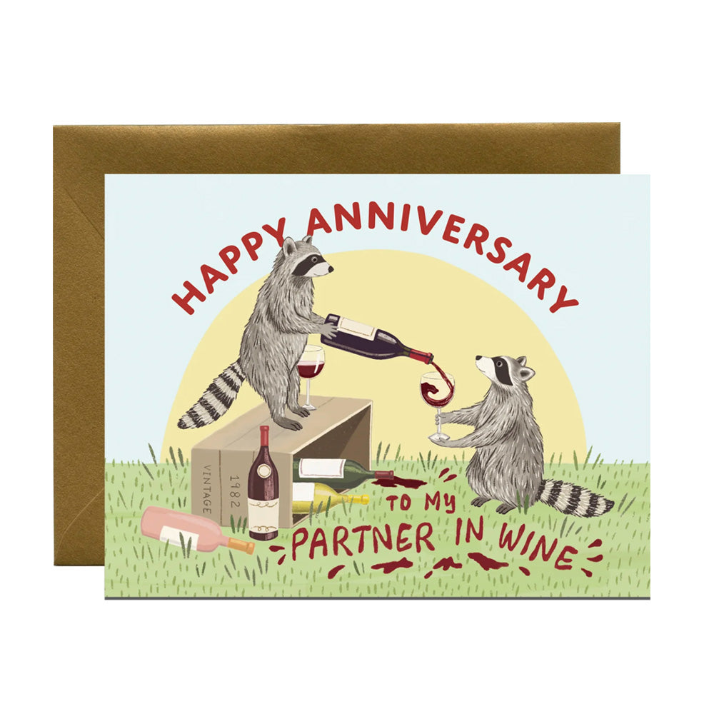 Card with two raccoons, spilled wine, on grass and text 'Happy Anniversary to my partner in wine' on a white background