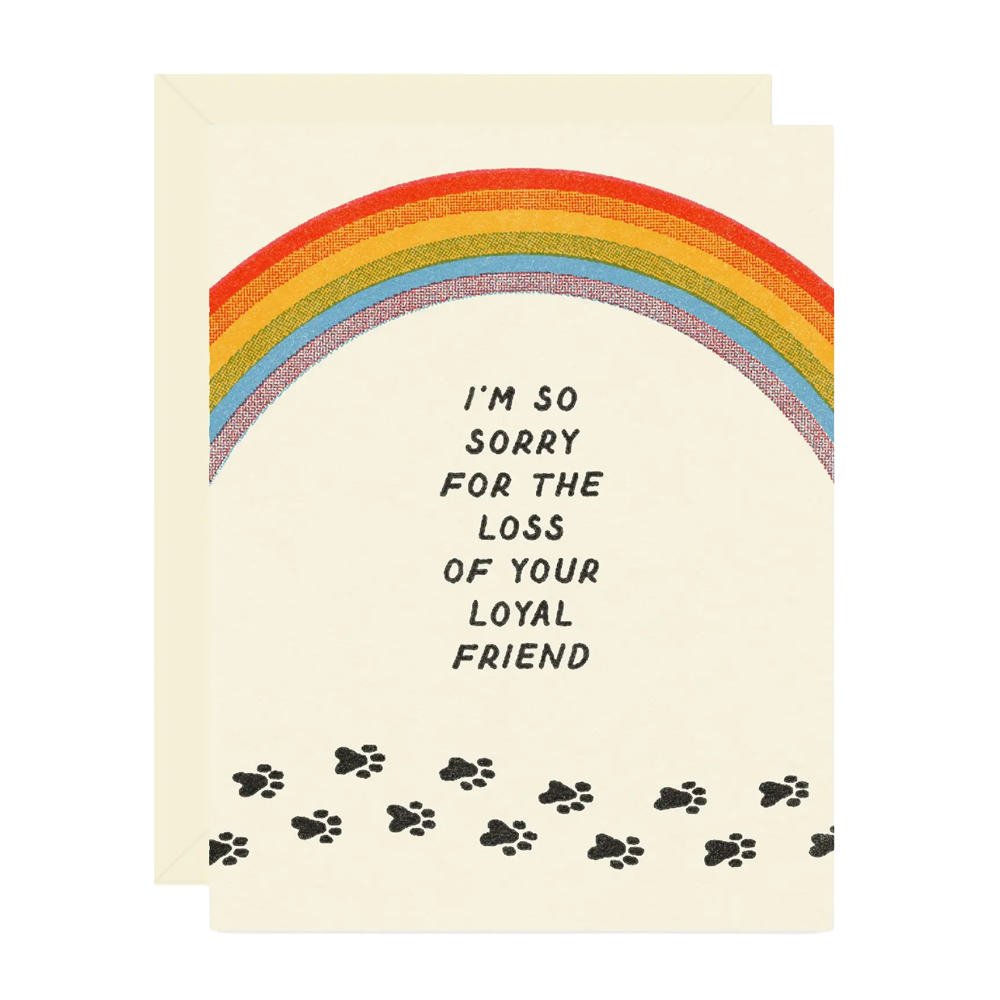 A cream-colored greeting card with a matching envelope, featuring a rainbow, the text 'I'M SO SORRY FOR THE LOSS OF YOUR LOYAL FRIEND' in black hand-lettered font, and black paw prints along the bottom.