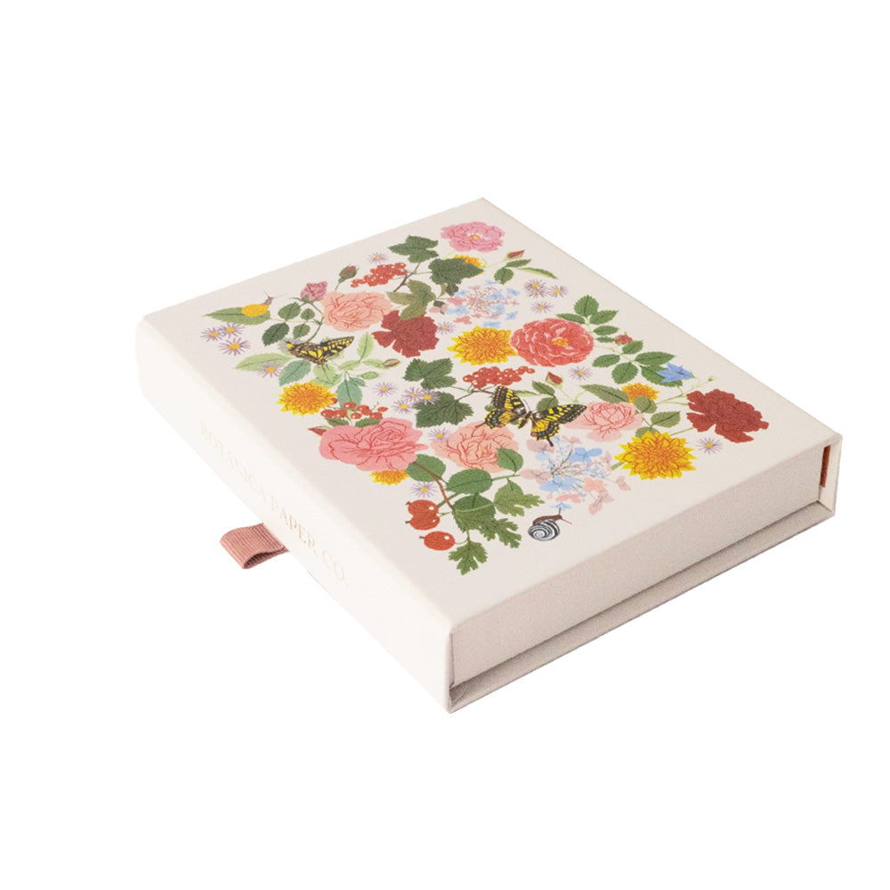 A cream card box with a fabric tab to open. The box has a floral background with butterflies on the top. 