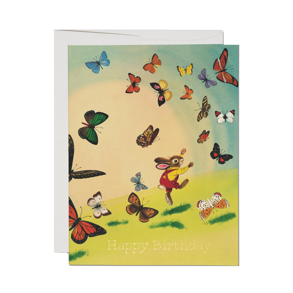 Birthday card with a rabbit and butterflies design on a white background. Light text in the grass on the bottom reads "Happy Birthday"