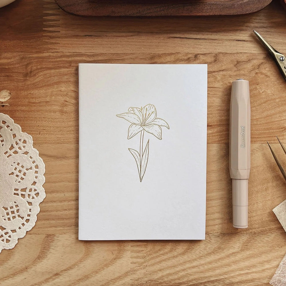 White notebook with floral design on a wooden surface with a pen and scissors.