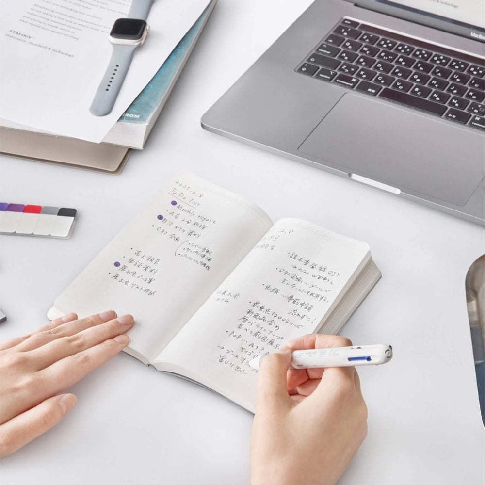 Person taking notes in a notebook with a laptop and stationery items on a desk