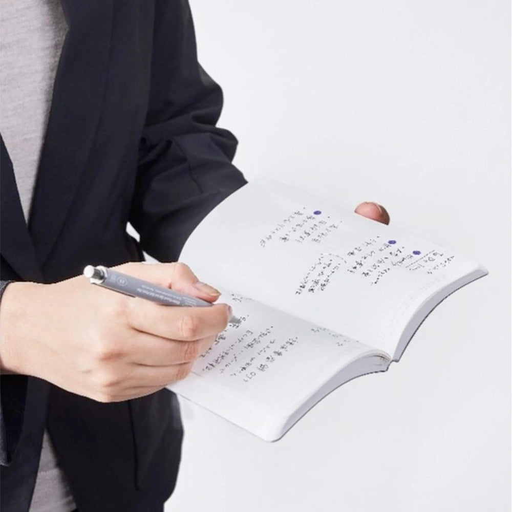 Person writing in a notebook with a pen on a light gray background