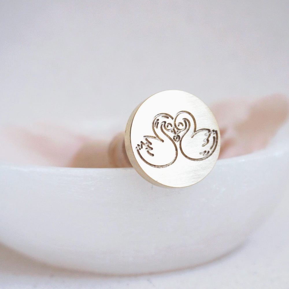 Gold wax seal head with two swans facing each other and kissing, making a heart