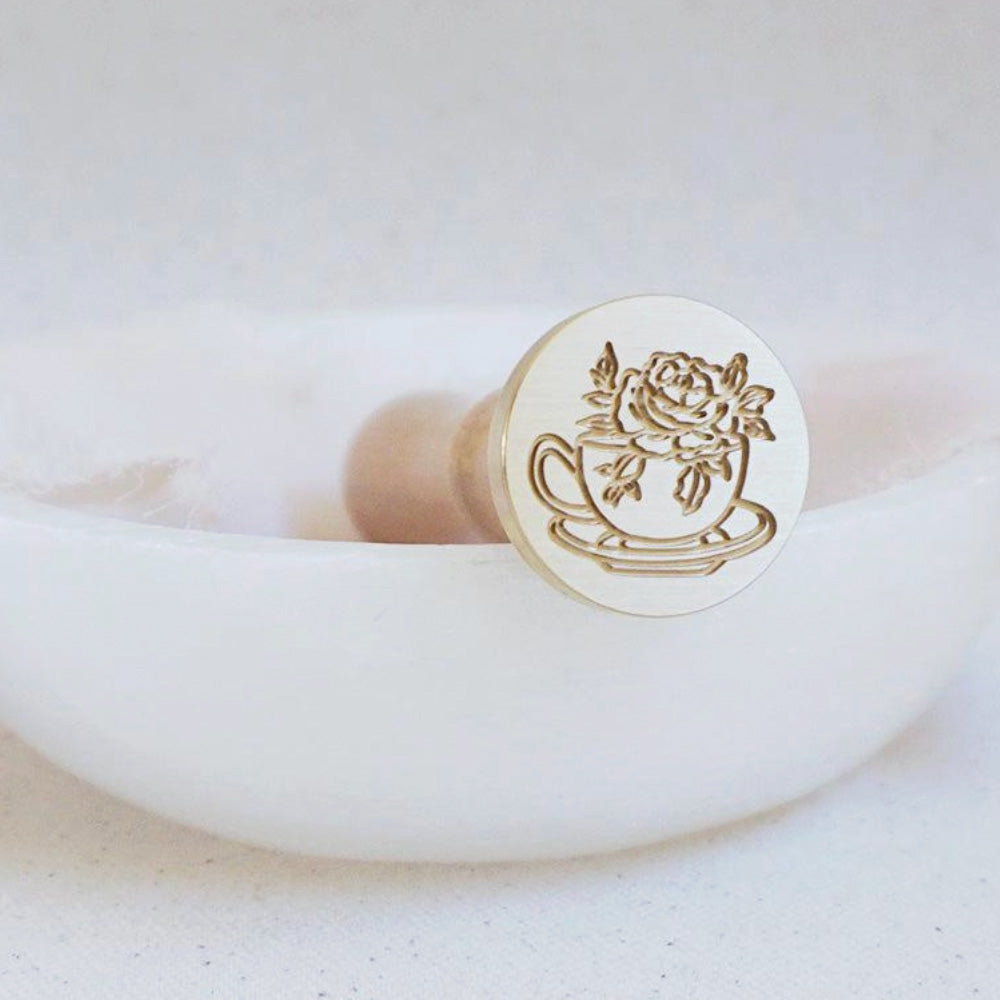 Gold wax seal head with teacup filled with a rose and leaves on a tea plate.