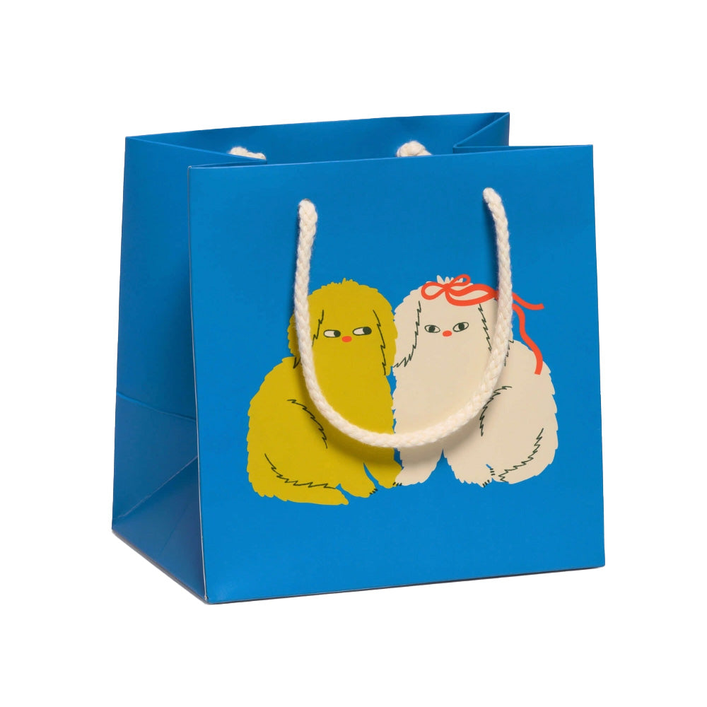 Blue gift bag with two cartoon dogs, one yellow and one white with a red bow, on a white background