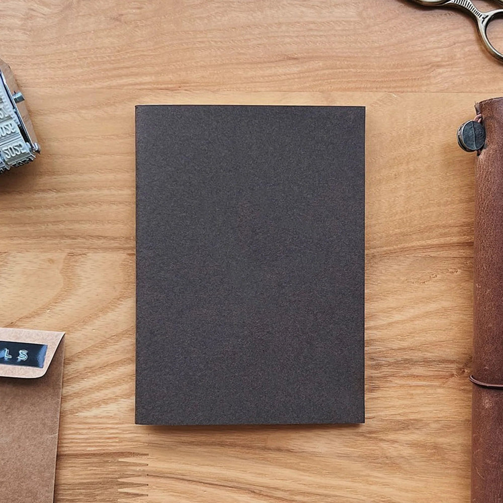 Dark gray notebook on a wooden surface with stationery items.