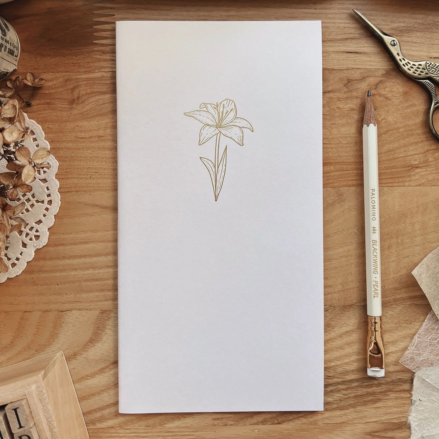 White notebook with floral design on a wooden surface with stationery items.