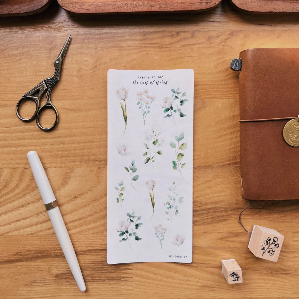 Stationery items including a pen, bookmark, scissors, and leather-bound notebook on a wooden surface.